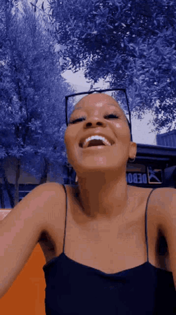 a woman with a bald head wearing glasses and a black tank top is smiling .