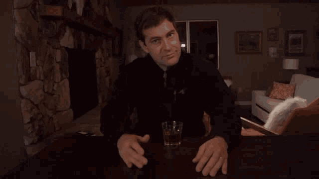 a man is sitting at a table with a glass of whiskey in front of him