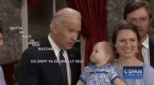 a man in a suit and tie is holding a baby in his arms while a woman looks on .