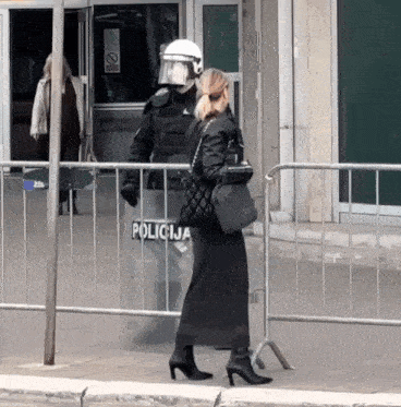 a woman walks past a police officer with a shield that says policija on it