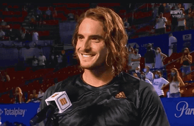 a man wearing a black adidas shirt is smiling in front of a microphone