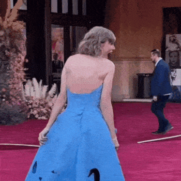 a woman in a blue dress is standing on a red carpet while a man in a suit stands behind her .