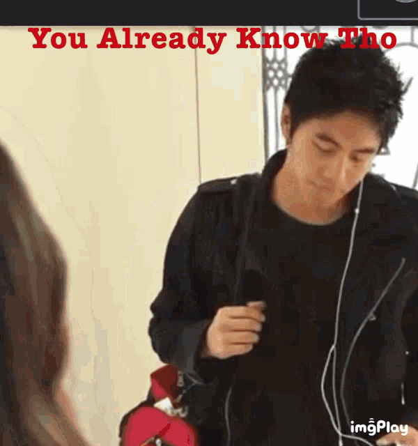 a man wearing ear buds and a black jacket with the words " you already know who " on the bottom