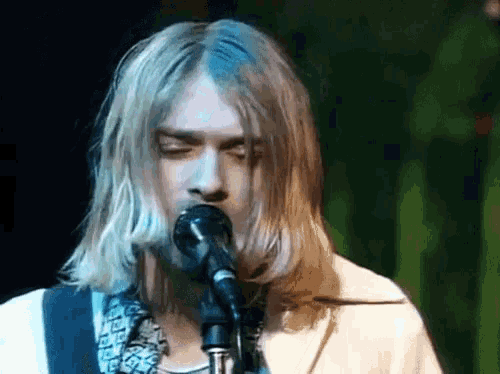 a man singing into a microphone with long blonde hair