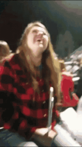 a woman in a red and black plaid shirt is laughing while holding a pencil .