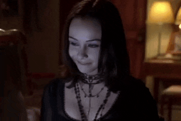 a woman with blue eyeshadow and a choker is smiling in a dark room with a lamp .