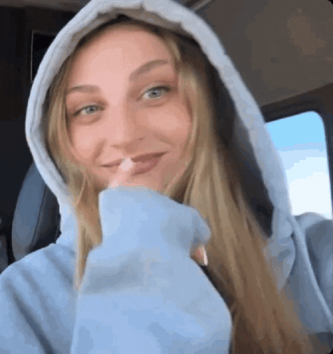a woman wearing a blue hoodie is taking a picture of herself in a car .