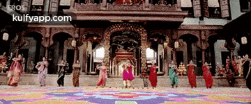 a group of people are dancing in front of a building with the words kulfyapp.com on the bottom .