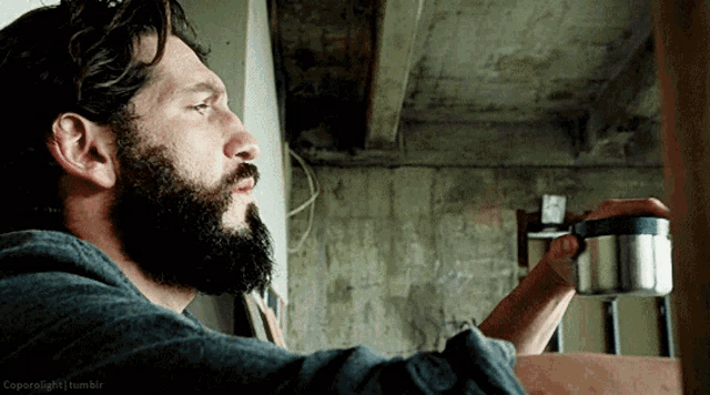 a man with a beard is drinking from a stainless steel cup ..