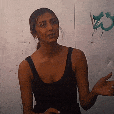 a woman in a black tank top stands in front of a wall with graffiti on it that says kc