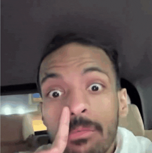 a man with a beard is making a funny face while sitting in the back seat of a car .