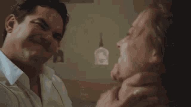 a man in a white shirt is holding a woman 's neck and smiling .