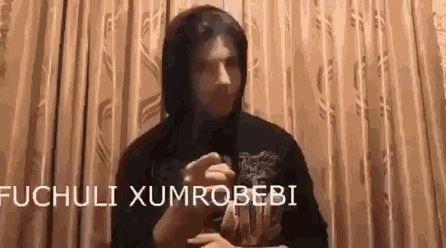 a man in a hoodie is standing in front of a curtain with the words ochuli xumrobebi written on the bottom