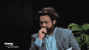 a man with a beard wearing a suit and blue shirt is pointing at something