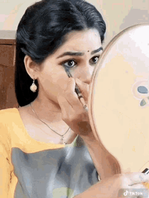 a woman is applying makeup to her face in front of a round mirror .