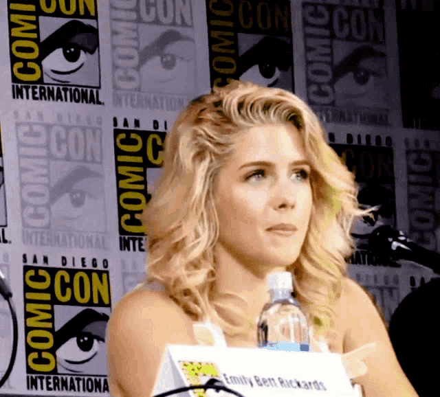 a woman stands in front of a wall with comic con logos on it