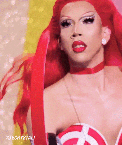 a drag queen with red hair is wearing a red choker and earrings .