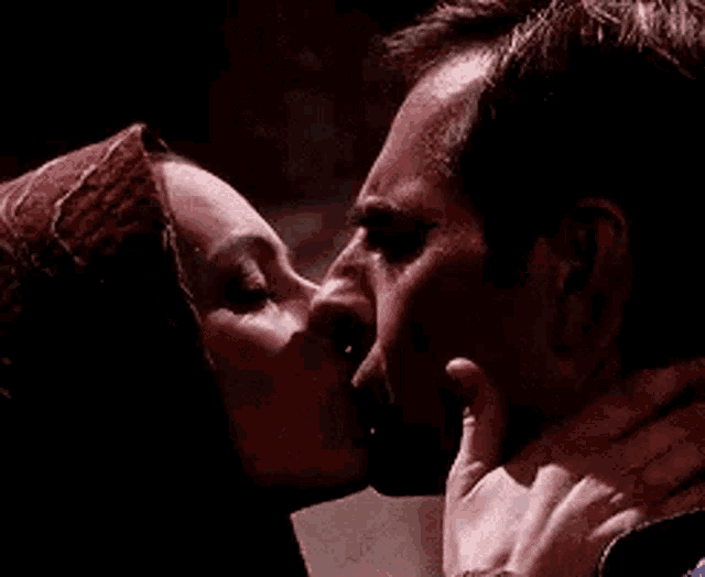 a man and a woman are kissing in a dark room and the woman is touching the man 's face .