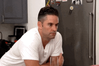 a man in a white shirt sits in front of a refrigerator with a magnet on it