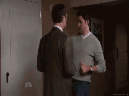 two men shaking hands in a hallway with a nbc logo on the wall