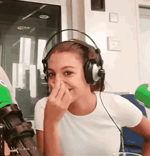a woman wearing headphones is sitting in front of a microphone and covering her nose .