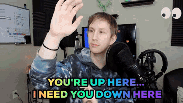 a man standing in front of a microphone with the words you 're up here i need you down here above him