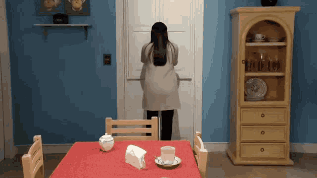 a woman in a white coat is standing in front of a door in a kitchen