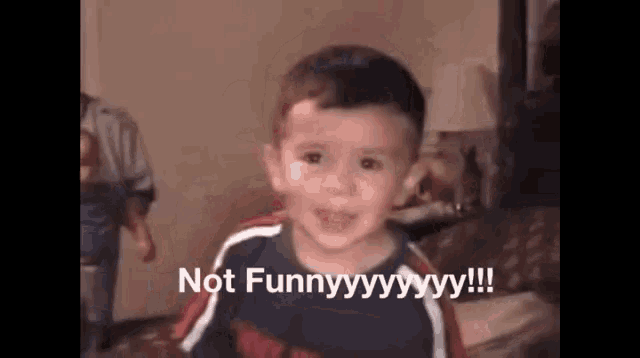 a young boy is sitting on a couch with the words " not funny " written on the screen behind him
