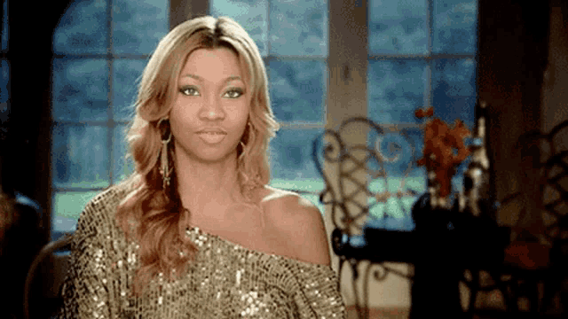 a woman in a gold sequined top is looking at the camera