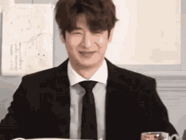 a man in a suit and tie is sitting at a table with a glass of water .