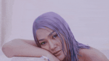 a woman with purple hair is sitting in a bathtub with her hands on her ears .
