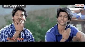 two young men are sitting next to each other in a park and smiling .