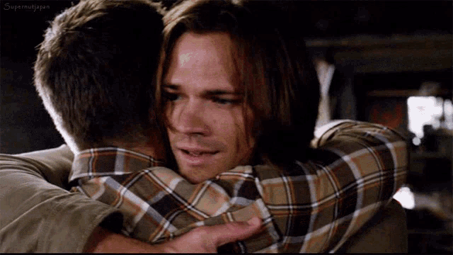 a man in a plaid shirt is hugging another man in a brown jacket