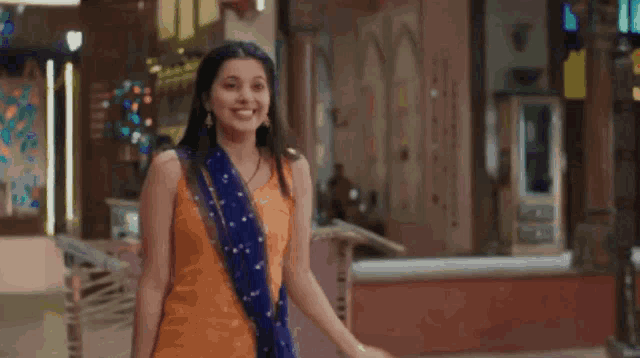 a woman in a yellow dress and blue scarf is dancing in a room with her arms outstretched .