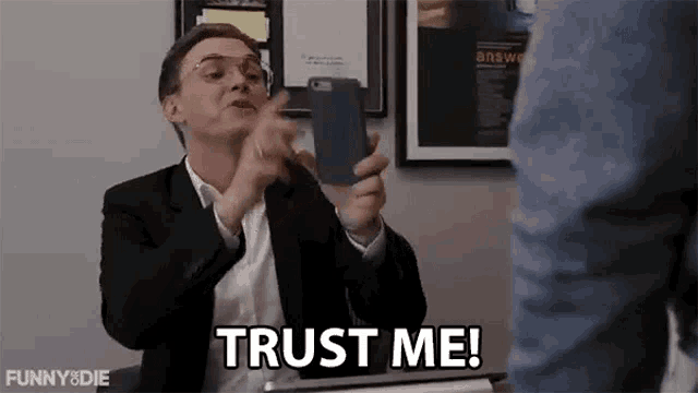 a man in a suit is holding a cell phone and saying `` trust me ! ''