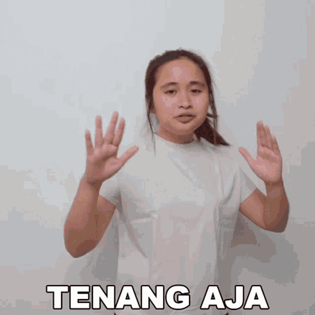 a woman in a white shirt is making a gesture with her hands and the words tenang aja written below her