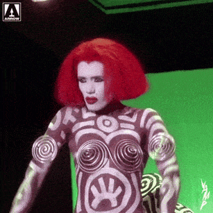 a woman with red hair and body paint stands in front of a green screen