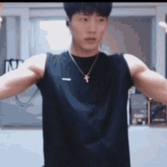 a man is flexing his muscles in front of a mirror while wearing a black tank top and a cross necklace .