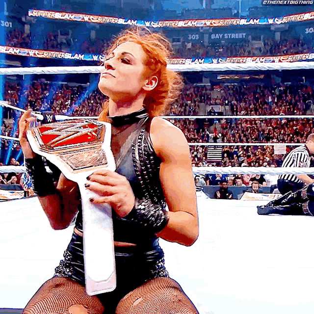 a female wrestler holds a trophy in front of a crowd that says summerslam on the banners