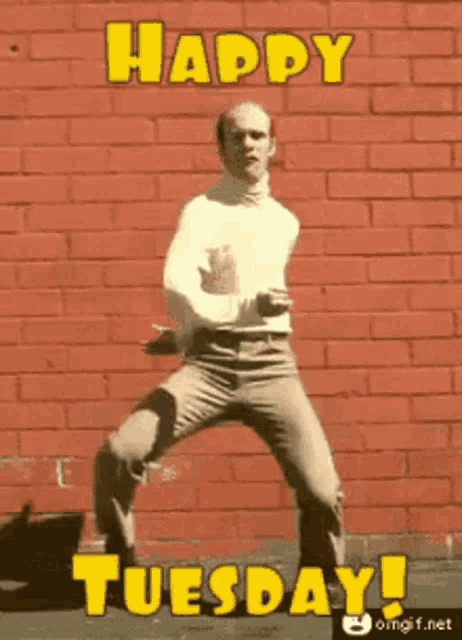 a man is dancing in front of a red brick wall with the words happy tuesday in yellow letters