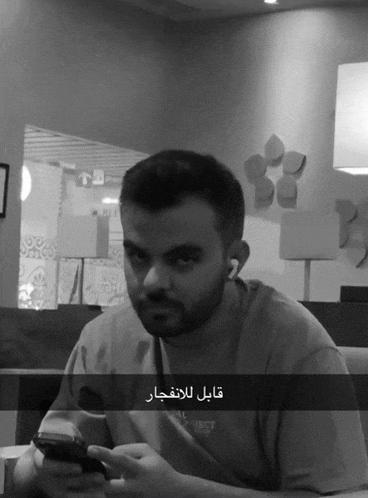 a man sitting at a table looking at a cell phone with arabic writing on the screen