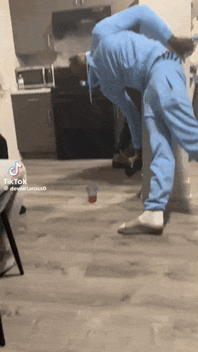 a man in a blue sweatsuit is doing a handstand in a kitchen with a cup on the floor