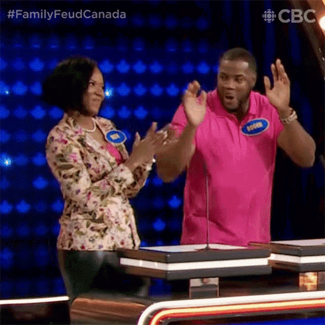 a man in a pink shirt is clapping with a woman in a floral jacket behind him .