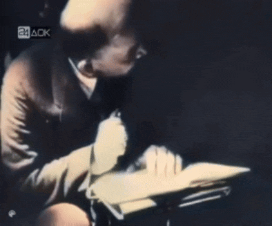 a man is writing on a piece of paper in front of a sign that says 24aok