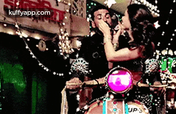 a woman is kissing a man on the cheek while riding a scooter .