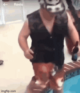 a man in a black vest and red shorts is standing next to a swimming pool .
