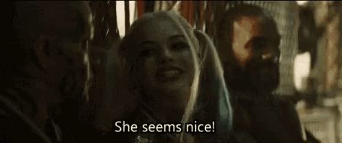 harley quinn from suicide squad is smiling and talking to two men while sitting next to each other .