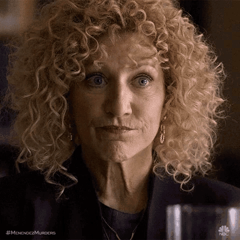 a woman with curly blonde hair is making a funny face while sitting at a table .