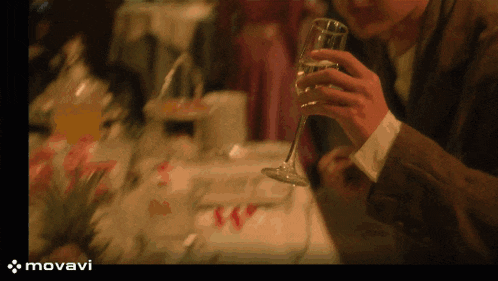 a man holds a glass of wine in front of a table with the word movavi on the bottom right