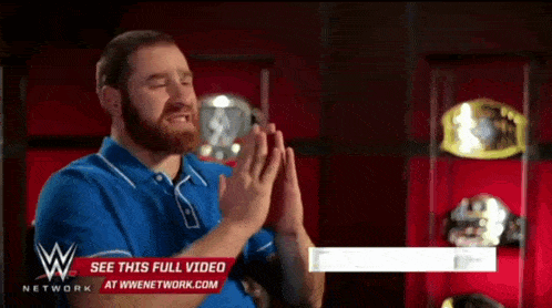 a man in a blue shirt is praying in front of a wall of wrestling trophies